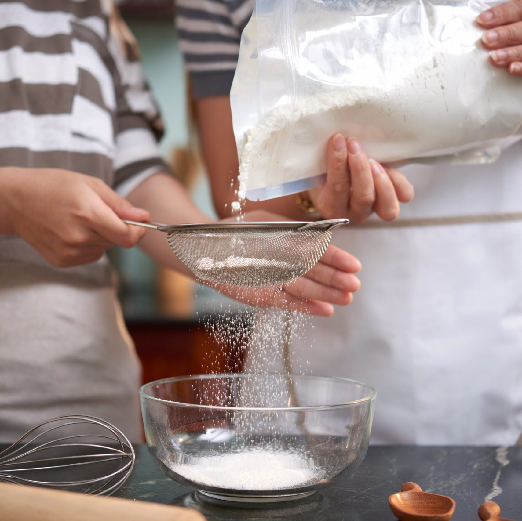 Crop shot of unrecognizable women sifting flour through sieve in kitchen while preparing cookie dough